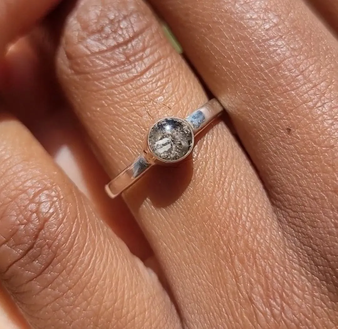 Silver ring with a round stone-set keepsake holding pet ashes, worn on a finger