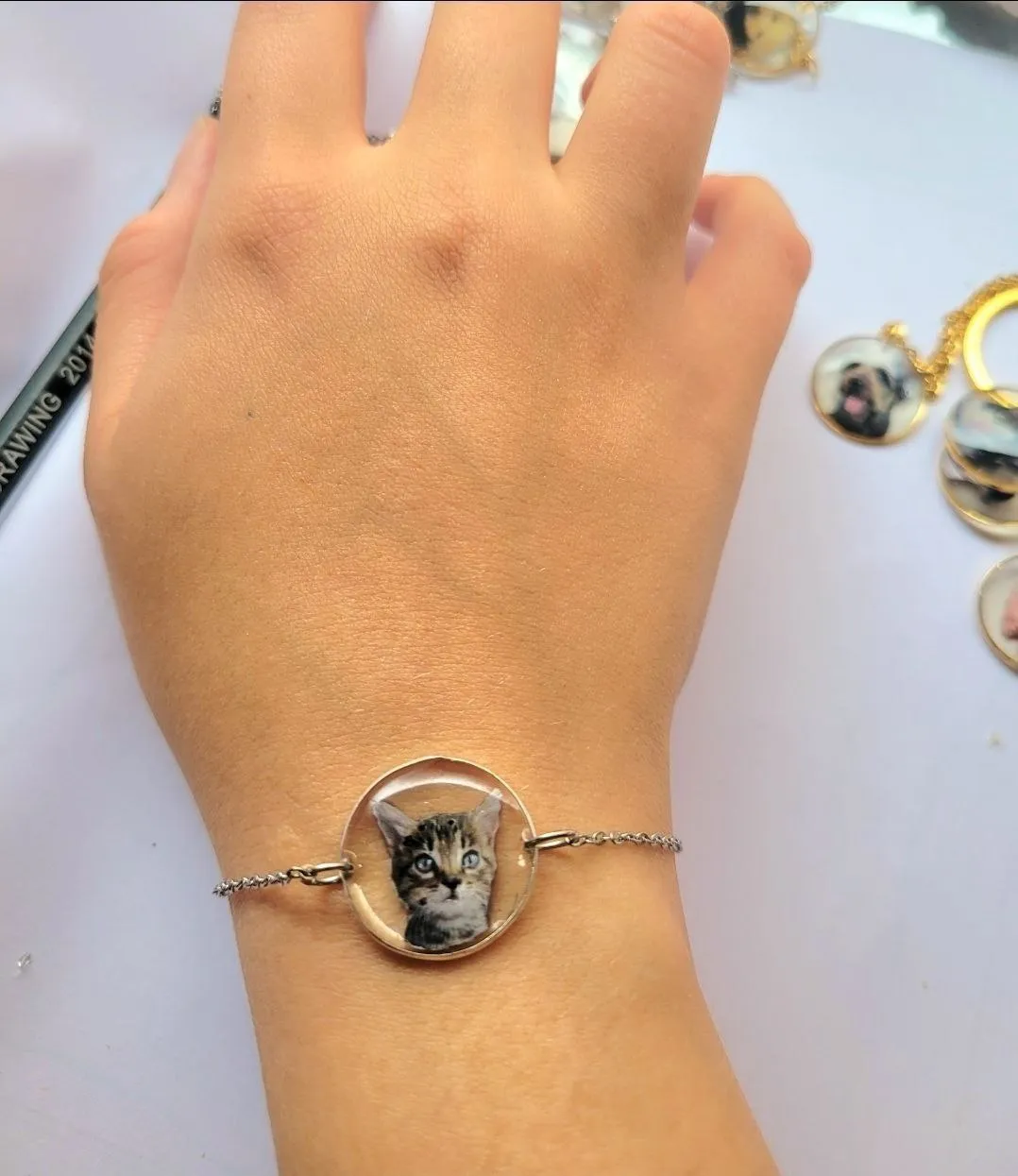 Chain bracelet with a round resin charm holding a kitten portrait, worn on a wrist