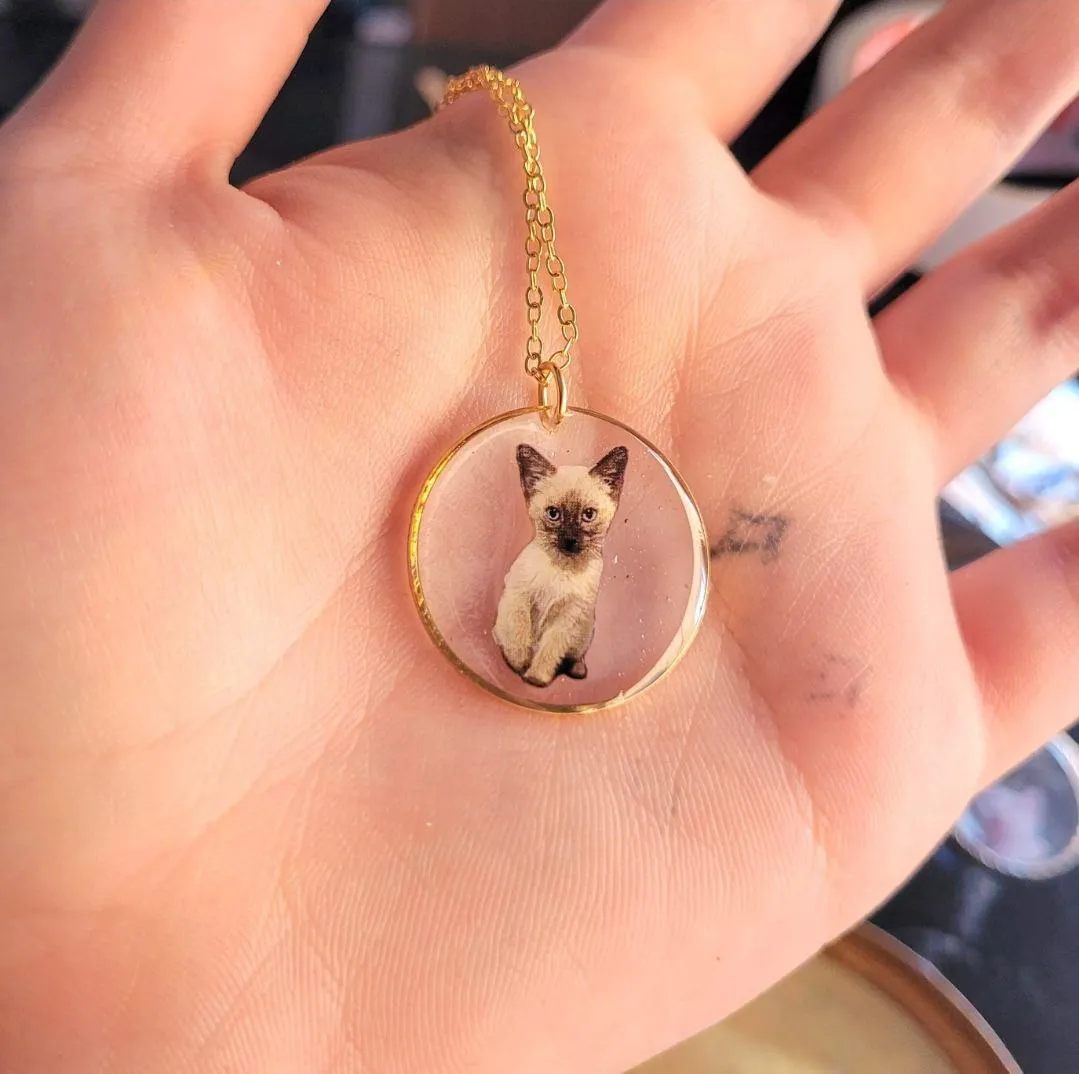 Gold necklace with a resin pendant holding a Siamese cat portrait, resting in a palm